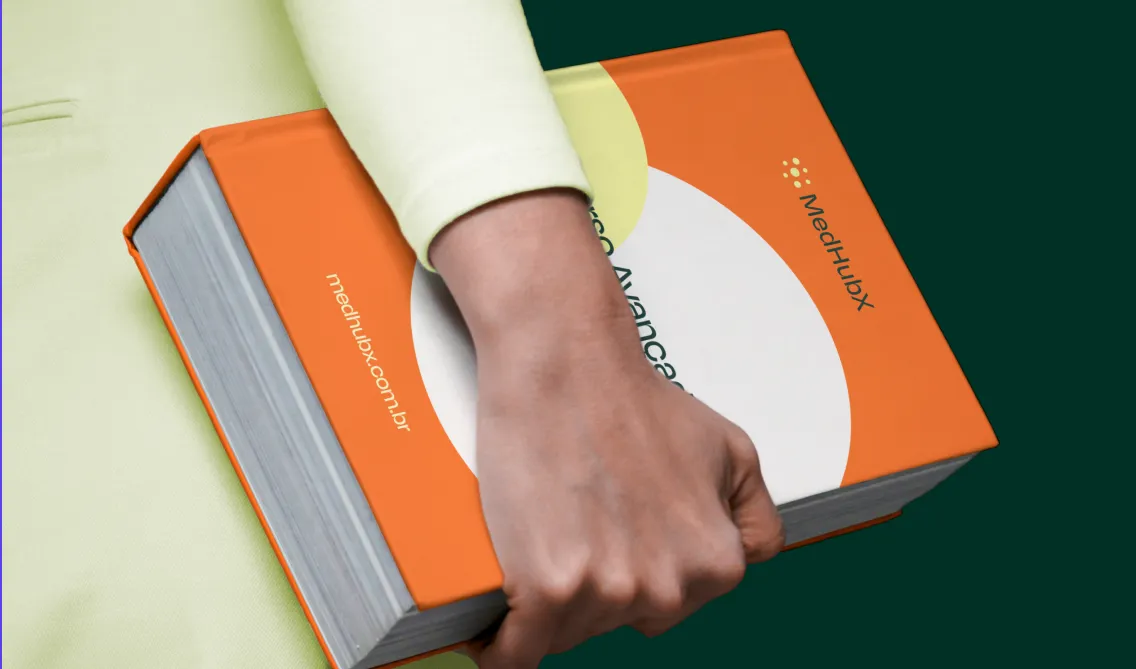 Mão segurando um livro da MedHubX, uma plataforma de educação médica inovadora, destacando a identidade visual da marca